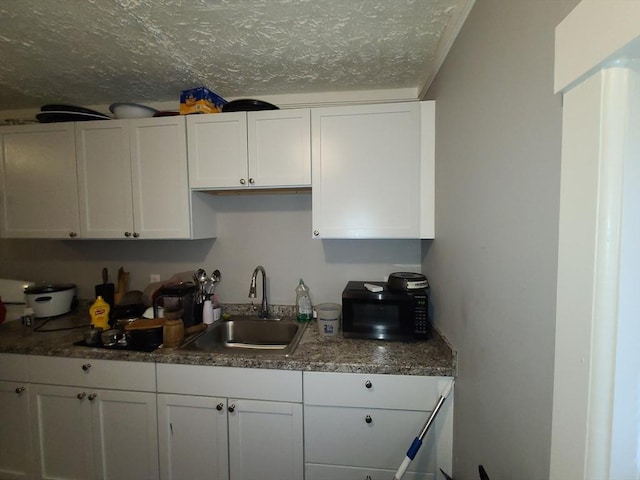 kitchen featuring a textured ceiling, white cabinets, and sink