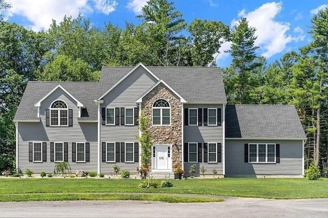 colonial home featuring a shingled roof, a front lawn, and stone siding