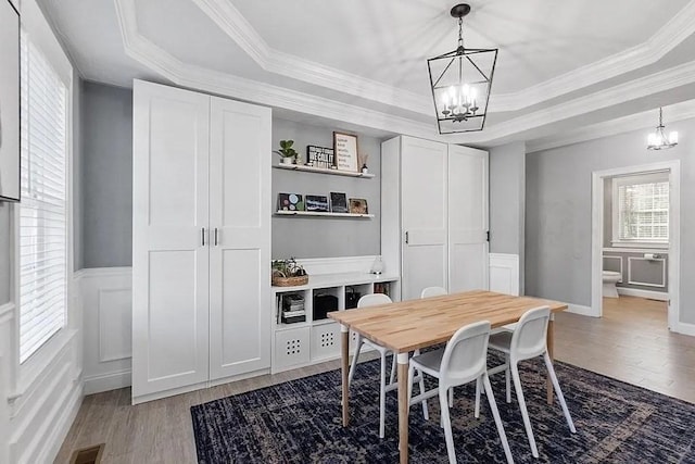 dining space with a raised ceiling, wood finished floors, and a notable chandelier