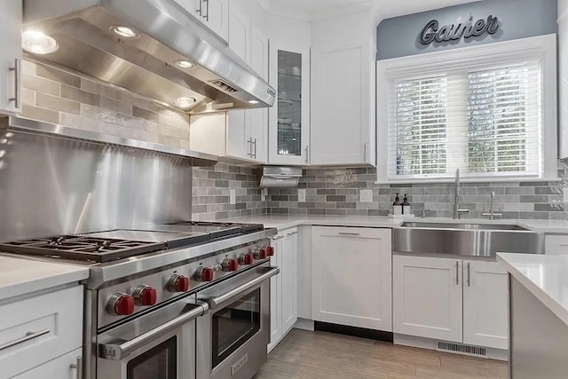 kitchen featuring light countertops, under cabinet range hood, white cabinets, range with two ovens, and a sink