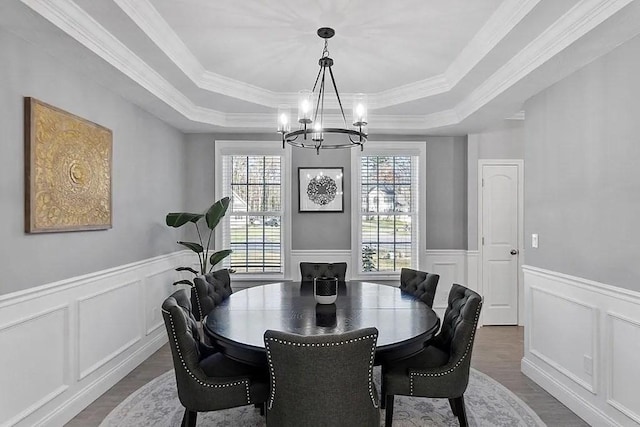 dining area with a decorative wall, dark wood-style floors, a wainscoted wall, a tray ceiling, and a notable chandelier