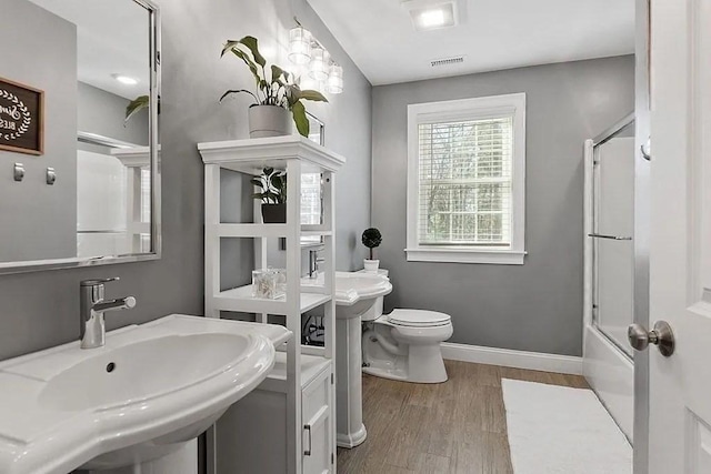 bathroom with wood finished floors, a sink, baseboards, combined bath / shower with glass door, and toilet