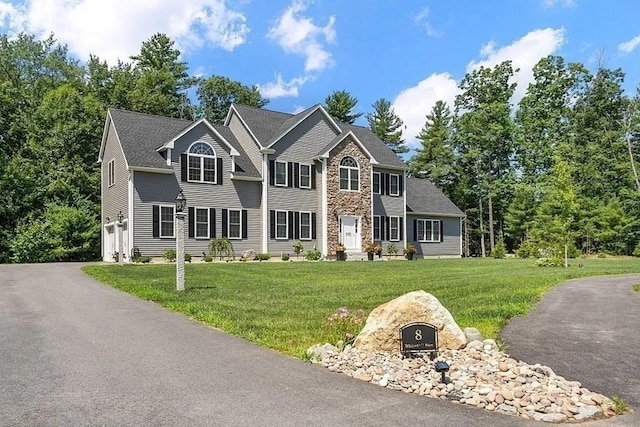 colonial home with an attached garage, aphalt driveway, stone siding, and a front yard