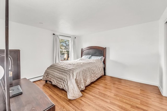 bedroom with a baseboard heating unit, baseboards, and light wood-type flooring