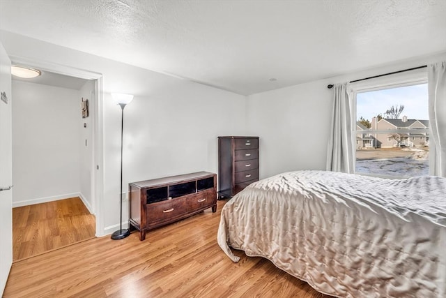 bedroom featuring light wood finished floors, a textured ceiling, and baseboards