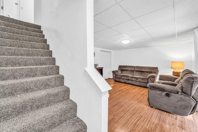 living room with stairs, a paneled ceiling, and wood finished floors