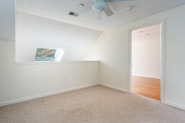 carpeted spare room with a ceiling fan, visible vents, vaulted ceiling, and baseboards