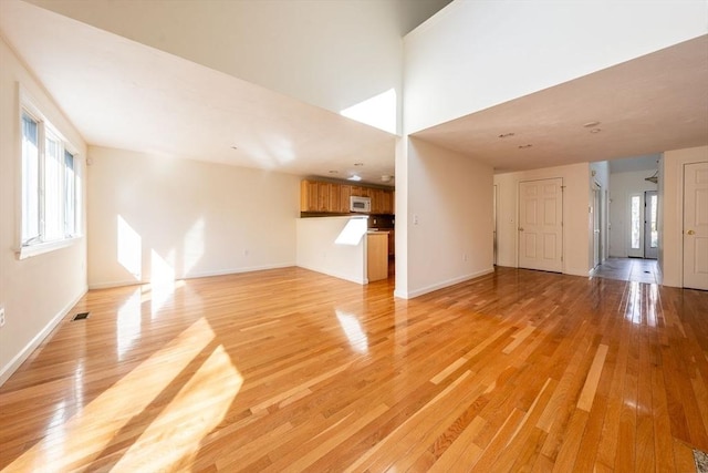 unfurnished living room featuring visible vents, light wood-style flooring, and baseboards