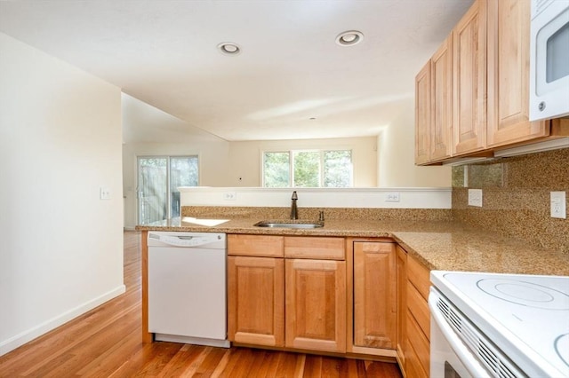 kitchen with light wood finished floors, a sink, white appliances, a peninsula, and baseboards