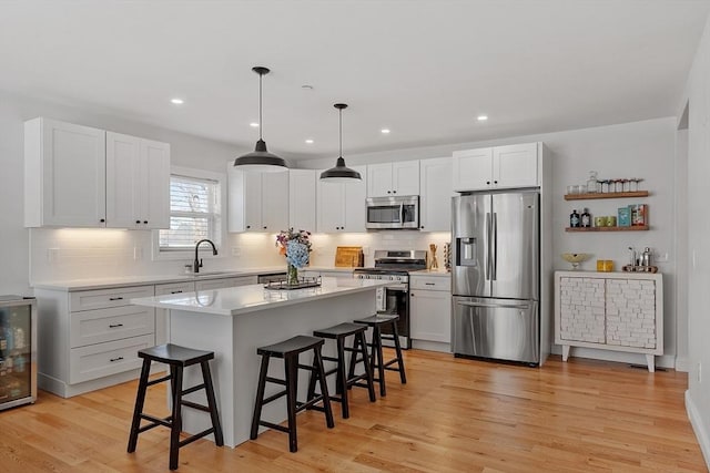 kitchen with sink, a breakfast bar, stainless steel appliances, white cabinets, and decorative light fixtures