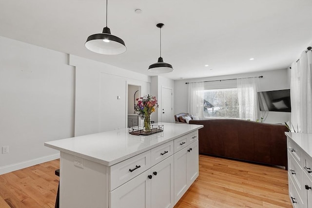 kitchen with hanging light fixtures, a kitchen island, white cabinets, and light wood-type flooring