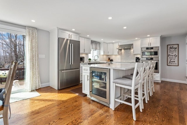 kitchen featuring white cabinetry, beverage cooler, a center island, stainless steel appliances, and wall chimney exhaust hood