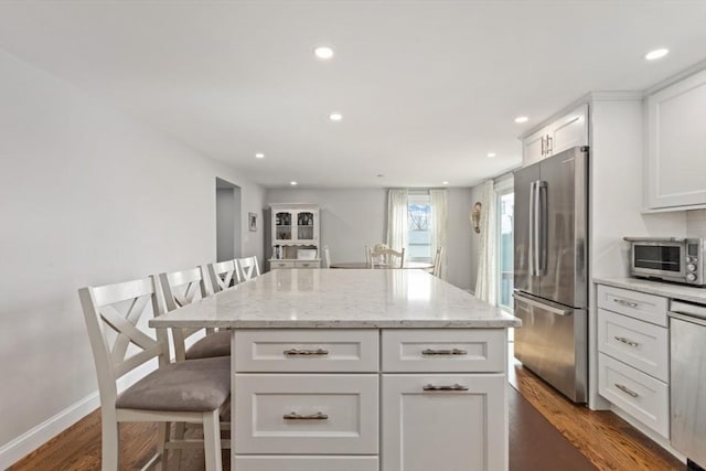 kitchen featuring a breakfast bar, white cabinetry, stainless steel fridge, a center island, and light stone counters