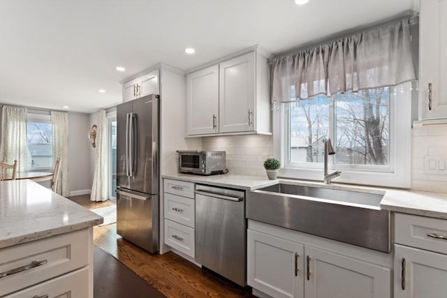 kitchen with white cabinetry, sink, light stone counters, stainless steel appliances, and dark wood-type flooring