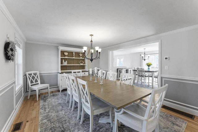 dining area with visible vents, an inviting chandelier, light wood-style flooring, and crown molding