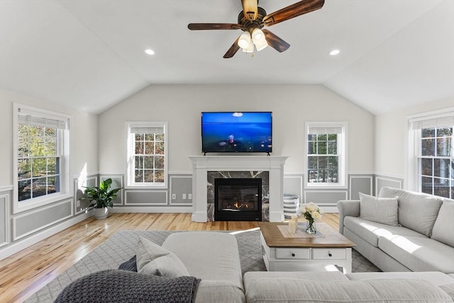 living area featuring vaulted ceiling, plenty of natural light, a fireplace, and a wainscoted wall