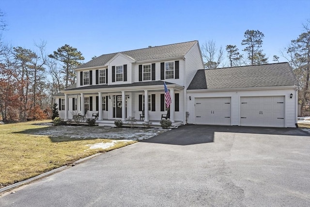 colonial home featuring a front yard, driveway, a porch, an attached garage, and a shingled roof