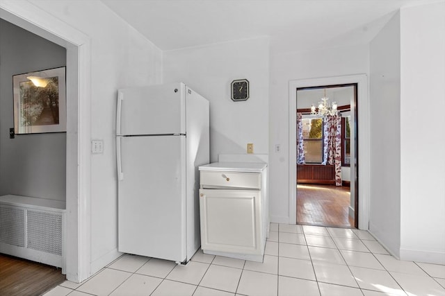 kitchen with an inviting chandelier, light tile patterned flooring, white cabinets, and white refrigerator