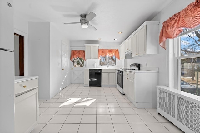 kitchen featuring radiator, a wealth of natural light, white cabinetry, black dishwasher, and white gas stove