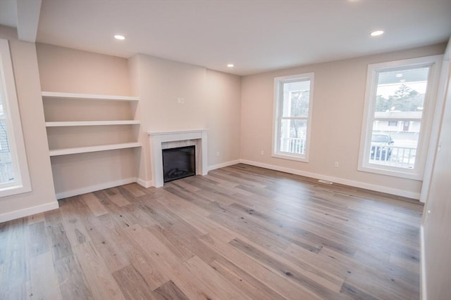 unfurnished living room featuring built in shelves, a wealth of natural light, and light hardwood / wood-style flooring