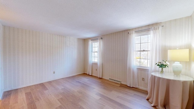 spare room featuring baseboard heating, a textured ceiling, and light wood-type flooring