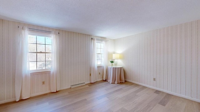 spare room with a baseboard radiator, a textured ceiling, and light wood-type flooring