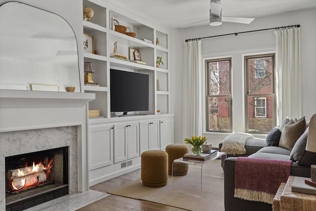 sitting room with a ceiling fan, visible vents, a premium fireplace, and wood finished floors