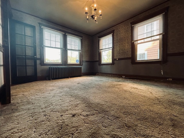 carpeted empty room featuring a chandelier, radiator heating unit, and a wealth of natural light