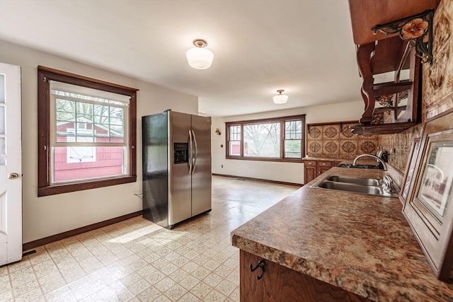 kitchen featuring stainless steel fridge, light flooring, a sink, baseboards, and dark countertops