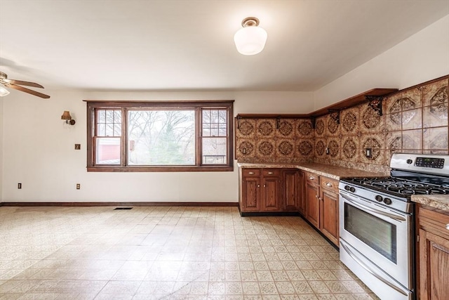 kitchen with gas range, brown cabinetry, a ceiling fan, and baseboards
