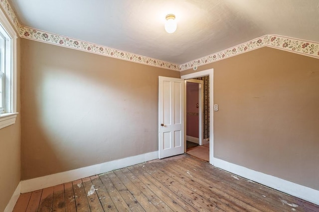 unfurnished room featuring hardwood / wood-style floors, baseboards, vaulted ceiling, and plenty of natural light