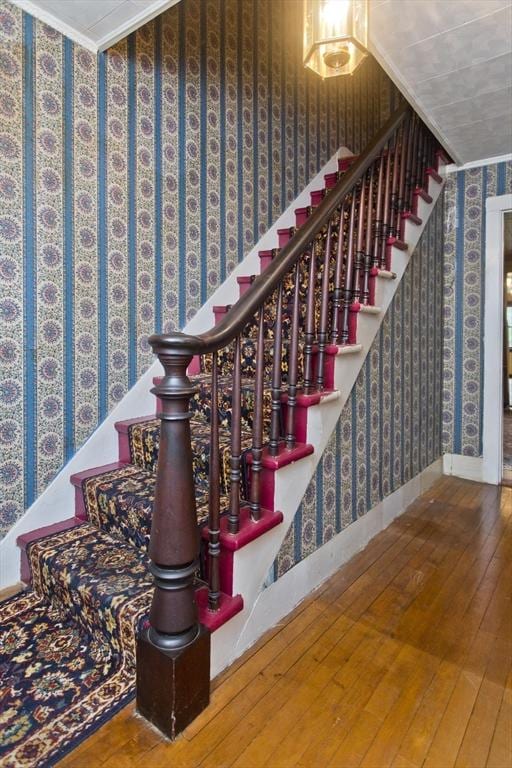 staircase with wallpapered walls, hardwood / wood-style flooring, crown molding, and baseboards