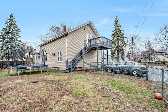 view of side of property featuring a chimney, a trampoline, a wooden deck, and a fenced backyard