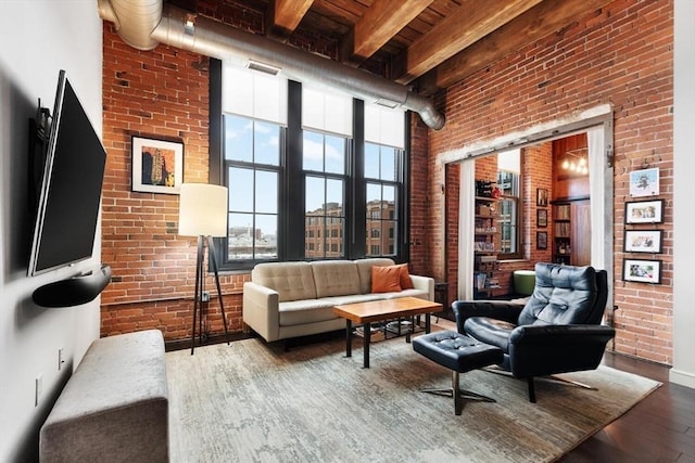 living area with brick wall, visible vents, a high ceiling, and wood finished floors