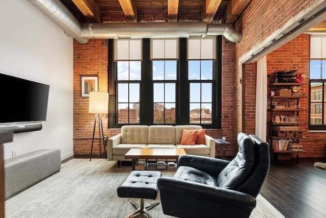 living area with baseboards, a towering ceiling, brick wall, and wood finished floors