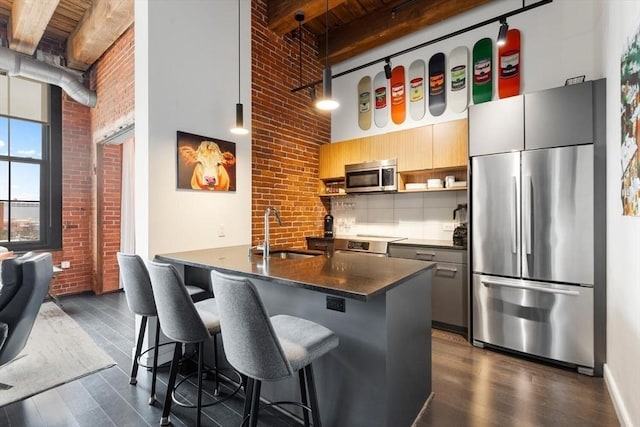 kitchen with dark countertops, brick wall, a high ceiling, stainless steel appliances, and a sink