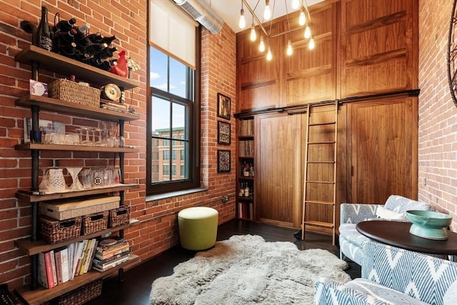 sitting room with a towering ceiling, brick wall, and wood finished floors