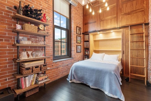 bedroom featuring hardwood / wood-style flooring, brick wall, and a high ceiling