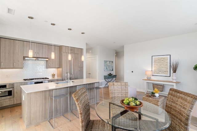 kitchen featuring appliances with stainless steel finishes, decorative light fixtures, sink, decorative backsplash, and light hardwood / wood-style floors