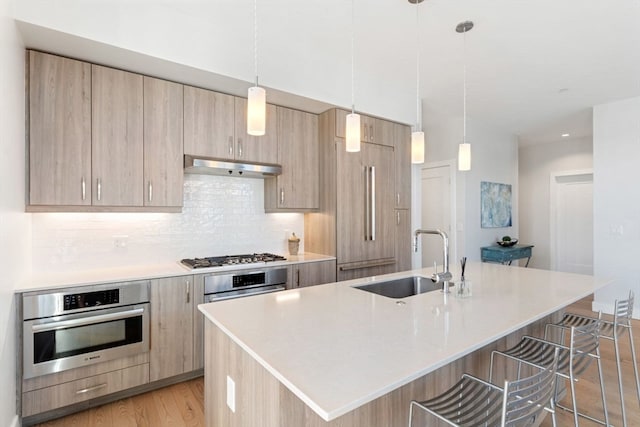 kitchen with appliances with stainless steel finishes, pendant lighting, light brown cabinetry, an island with sink, and sink