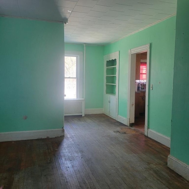 empty room with built in features, wood-type flooring, and baseboards