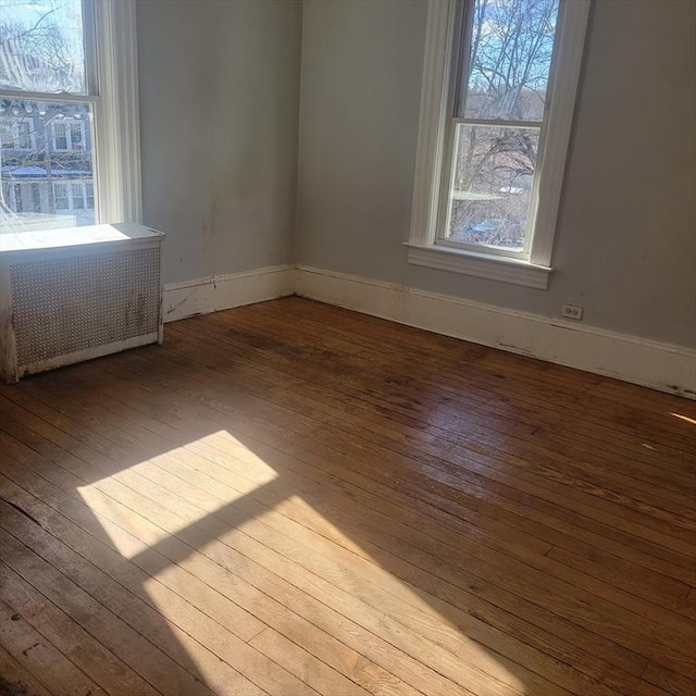 unfurnished room with baseboards, wood-type flooring, and radiator