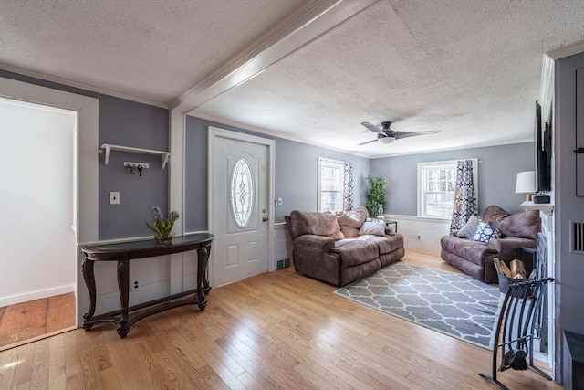 living room with ceiling fan, a textured ceiling, light wood-type flooring, ornamental molding, and visible vents