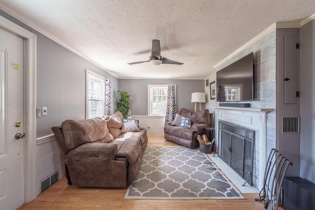 living room featuring light wood-style flooring, crown molding, ceiling fan, and a textured ceiling