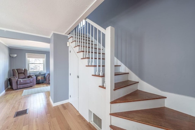 stairs with crown molding, wood finished floors, a wood stove, and visible vents