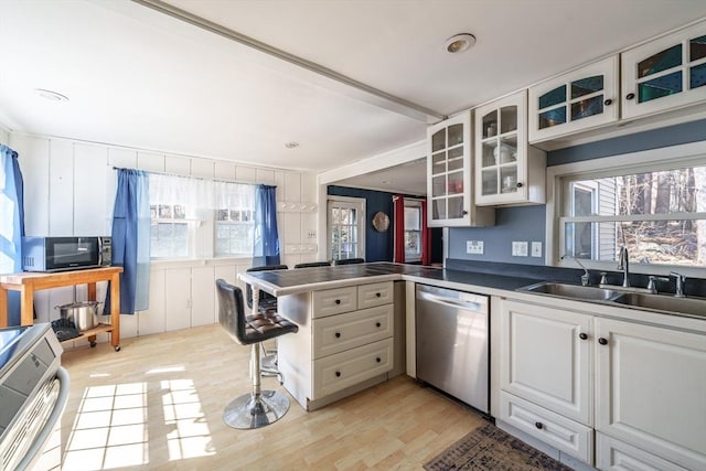 kitchen with black microwave, a peninsula, light wood-style floors, stainless steel dishwasher, and a sink
