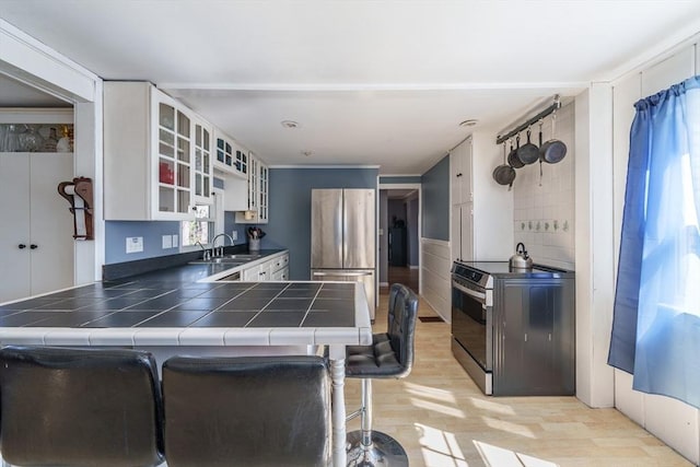 kitchen with light wood-style floors, a peninsula, a sink, stainless steel appliances, and tile counters