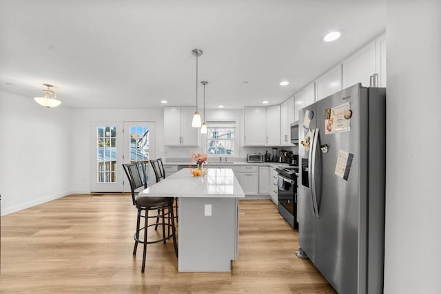 kitchen featuring decorative light fixtures, a kitchen island, white cabinets, and appliances with stainless steel finishes