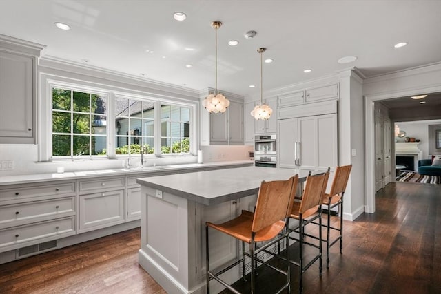 kitchen with a kitchen island, sink, a kitchen bar, hanging light fixtures, and ornamental molding