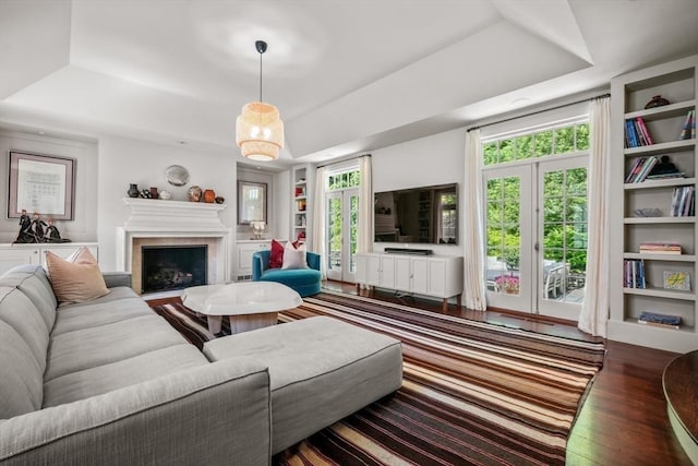 living room with dark hardwood / wood-style floors, plenty of natural light, a tray ceiling, and built in features